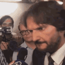 a man in a suit and tie is talking into a microphone while another man takes a picture of him .
