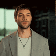 a man with a beard wearing a suit and a necklace with a square pendant