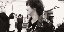 a black and white photo of a man in a studded jacket standing in front of a microphone .