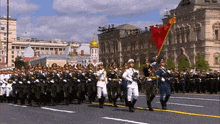 a group of soldiers marching in a parade with a red flag