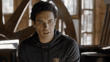a young man in a black hoodie is sitting in a room looking at the camera .