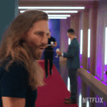 a man with long hair and a beard is standing in a hallway with netflix written on the bottom right