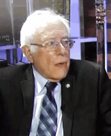 a man wearing glasses and a suit is talking on a microphone