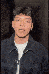 a young man wearing a black jacket and a white shirt is making a face .