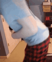 a person wearing a blue shirt and red plaid pants is standing in a room with boxes on the wall .