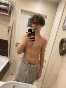 a young man wrapped in a towel takes a selfie in a bathroom mirror