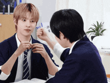 two young men are sitting at a table and one of them is adjusting another man 's tie