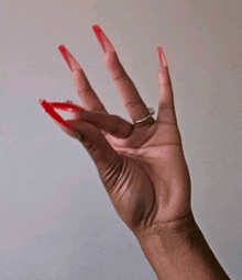 a woman 's hand with very long red nails and a silver ring