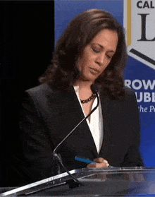 a woman in a suit is sitting at a podium with a microphone and a pen in her hand .
