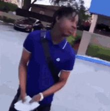 a man in a blue shirt is standing in a parking lot holding a piece of paper in his hand .