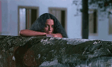 a woman with long hair is leaning on a stone wall .
