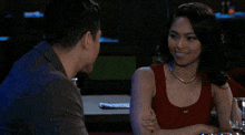 a man and a woman are sitting at a table and the woman is wearing a red tank top
