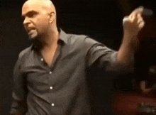 a bald man in a black shirt is standing in front of a microphone .