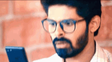 a man with glasses and a beard is looking at his phone .