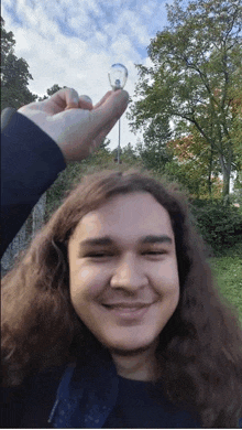 a young man with long hair is smiling while holding a light bulb in his hand