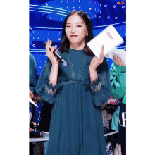 a woman in a blue dress holds a microphone and a piece of paper