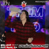 a man in a red plaid shirt is drinking from a bottle in front of a sign that says big love