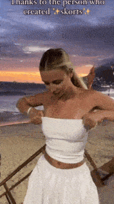 a woman wearing a white top and skirt is standing on a beach .