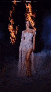 a woman in a long dress is standing in front of a fire .