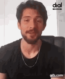 a man with a beard and a chain around his neck is sitting in a chair and smiling .
