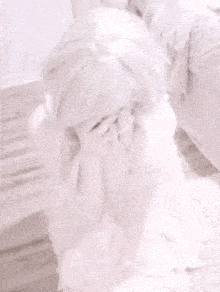 a woman in a white dress is covering her face with her hands while sitting on a couch .