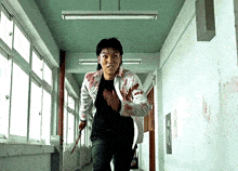 a man in a bloody shirt is running down a hallway with a knife .