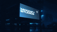 a large billboard for modify studios is lit up in the rain