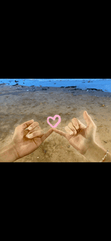 a couple making a pink heart with their fingers on a beach