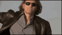 a man wearing sunglasses and a leather jacket is standing in the desert
