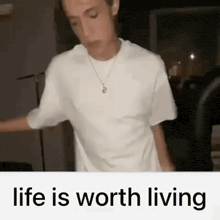 a man in a white t-shirt is dancing in a dark room with the words `` life is worth living '' .