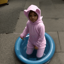 a little girl in a pink hoodie is kneeling in a blue pool of water