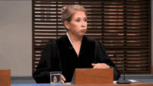 a female judge sits in front of a microphone with a glass of water in front of her