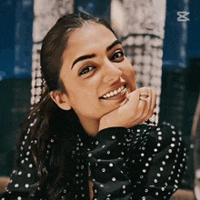 a woman wearing a black polka dot shirt is smiling with her hand on her chin