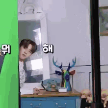 a man is standing in front of a green screen in a room with a dresser and a phone on it .
