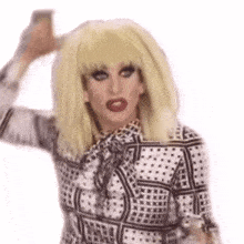 a drag queen wearing a wig and a polka dot shirt is holding a glass of wine .
