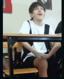 a boy sits at a desk with his hands on his knees