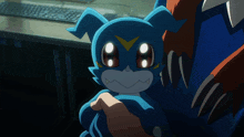 a person is holding a small blue monster with a yellow triangle on its face