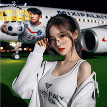 a woman wearing a mio paly shirt stands in front of a mixipal airplane