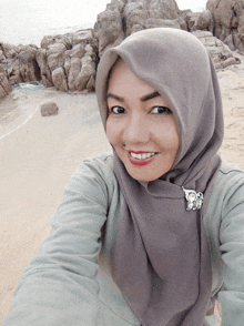 a woman wearing a hijab and a brooch smiles for a picture