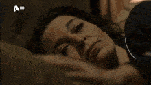 a black and white photo of a man laying on a bed covering his face with his hands .