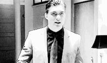 a man in a suit and tie is standing in front of a lamp in a black and white photo .
