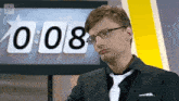 a man in a suit and tie stands in front of a clock that reads 0 : 08