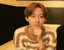 a young man wearing a striped sweater has his hand to his chin