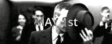 a man in a suit and tie is holding a hat in front of his face and the date may 1st is written above him