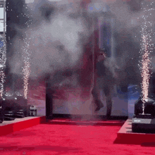 a man walking on a red carpet with smoke coming out of it