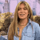 a woman with long blonde hair is wearing a blue denim shirt and a gold necklace .
