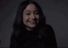 a woman with long dark hair is smiling and wearing a black turtleneck