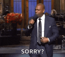 a man in a suit and tie is standing in front of a microphone and says sorry .