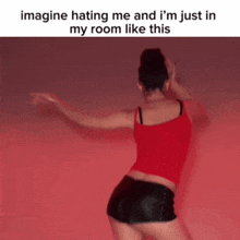 a woman in a red tank top and black shorts is dancing in front of a red wall ..