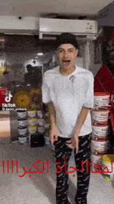 a man wearing a white shirt and black pants is standing in front of buckets of paint ..